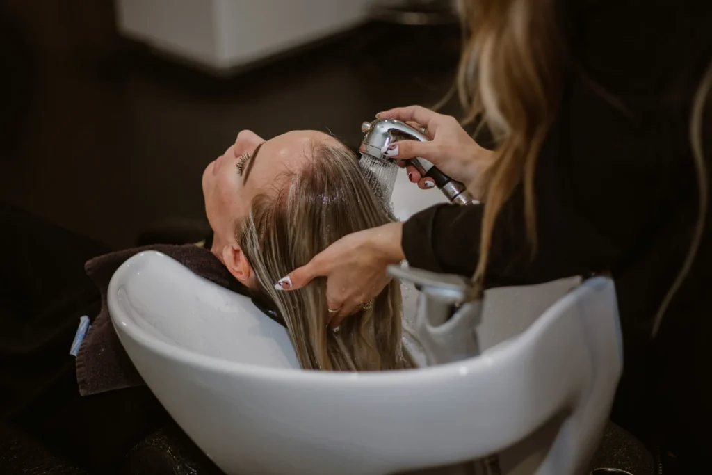 Kobieta siedzi na fotelu, a fryzjer strzyże jej włosy nożyczkami w salonie.