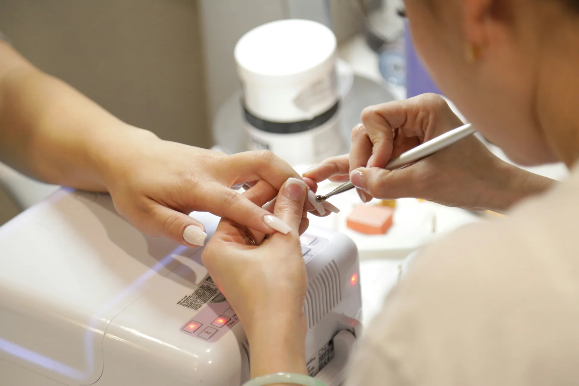 Kobieta w salonie kosmetycznym, gdzie stylistka paznokci wykonuje jej manicure hybrydowy.