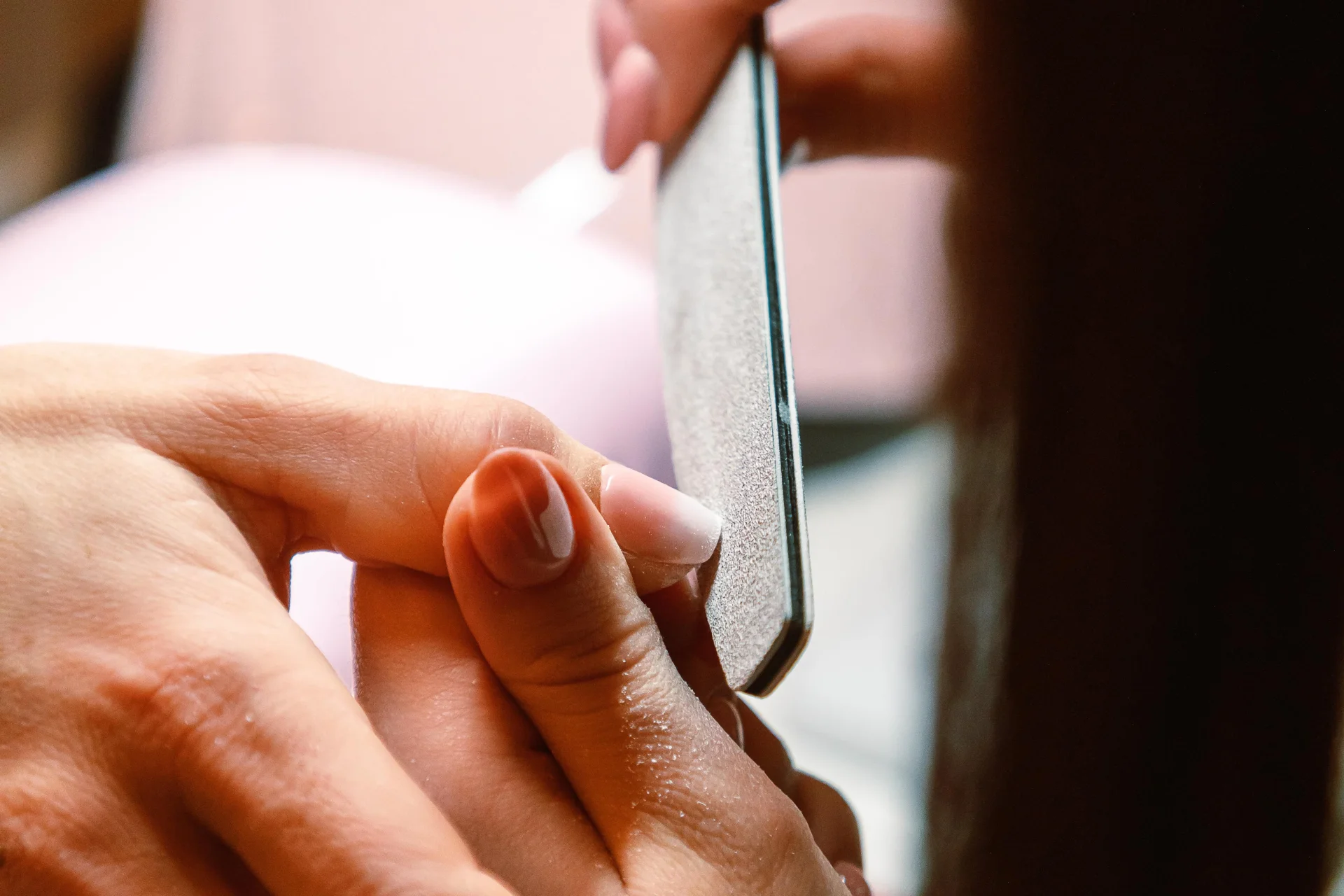 Zbliżenie na profesjonalną sesję manicure, podczas której kosmetyczka używa pilnika do paznokci.