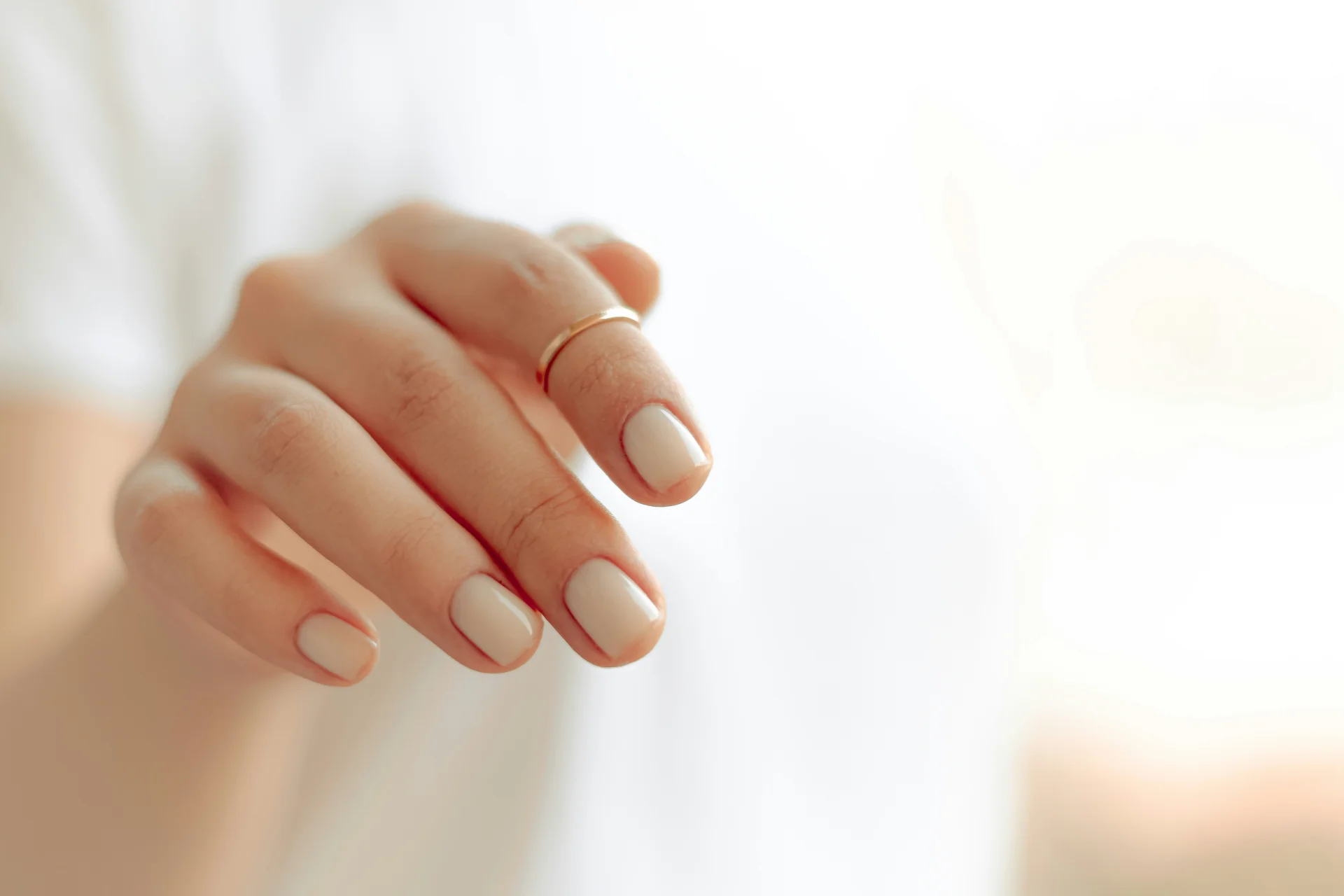 Zbliżenie na dłoń osoby z eleganckim, białym manicure, prezentującym zadbane paznokcie.