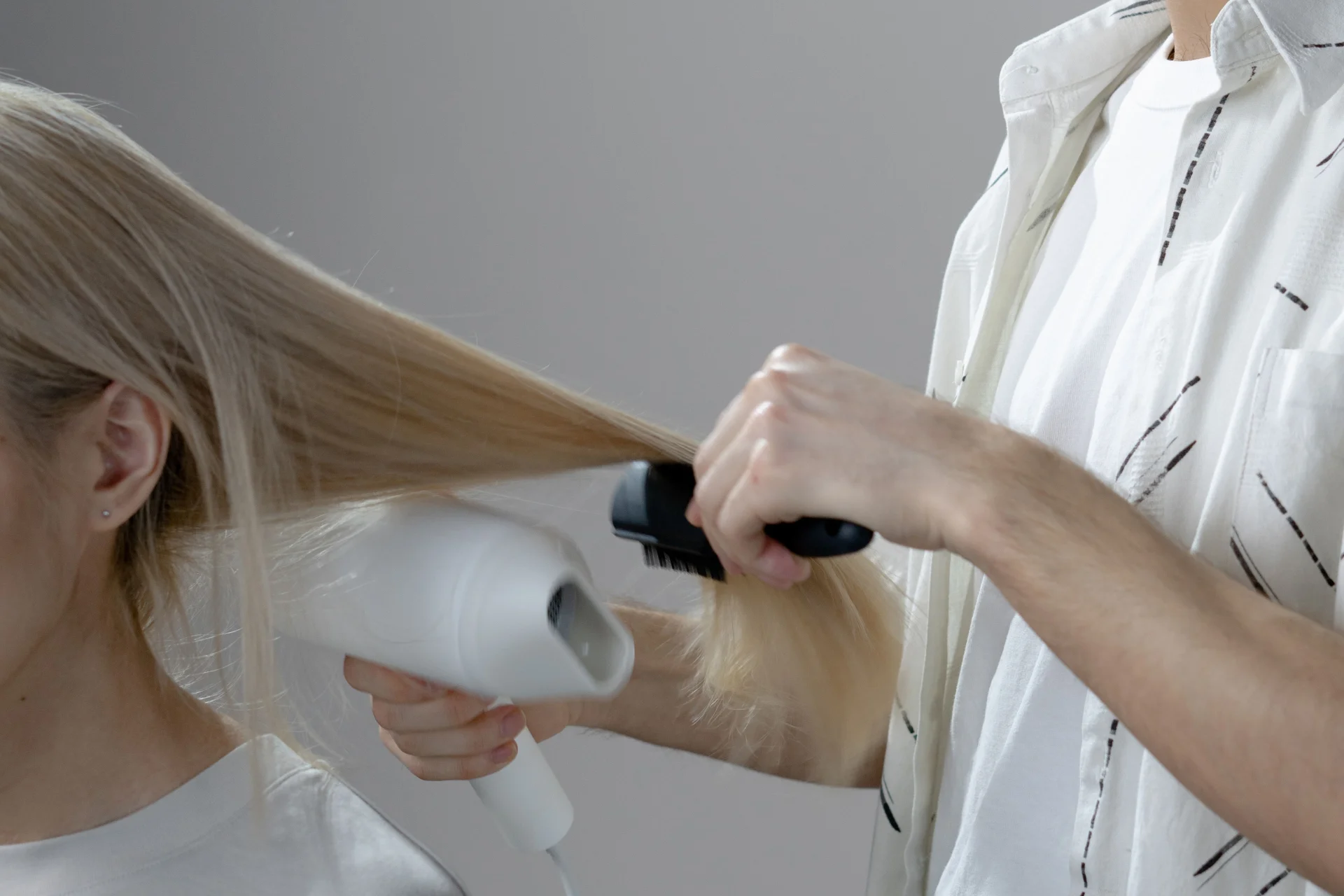 Fryzjer stylizuje długie blond włosy klientki suszarką i szczotką w salonie fryzjerskim.